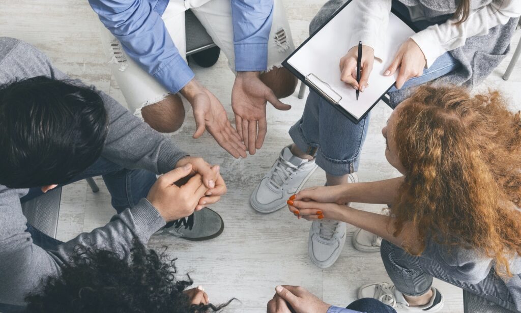 Diverse people sharing their problems at group therapy session, top view